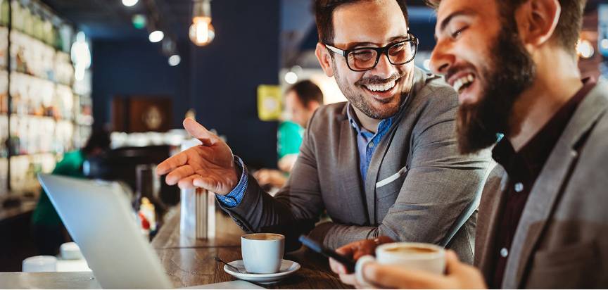 hommes souriant et discutant devant un café et un ordinateur